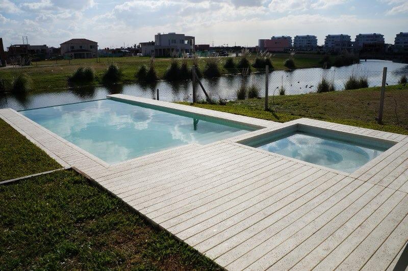 Piscina con jacuzzi climatizado y desborde infinito hacia el arroyo, solárium en listón de deck